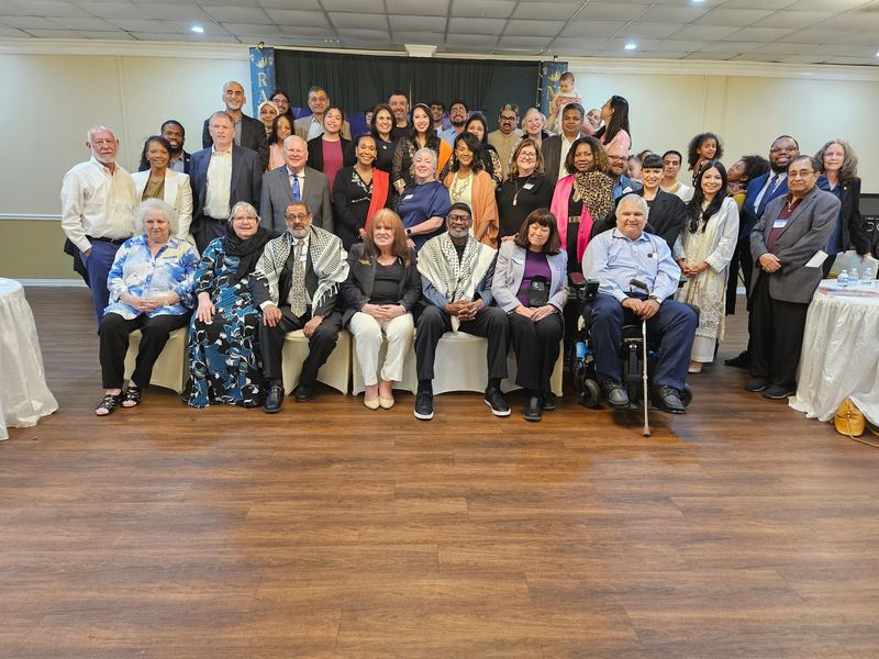 Large group photo at a Ramadan Iftar dinner in a banquet hall, several guests wearing keffiyehs