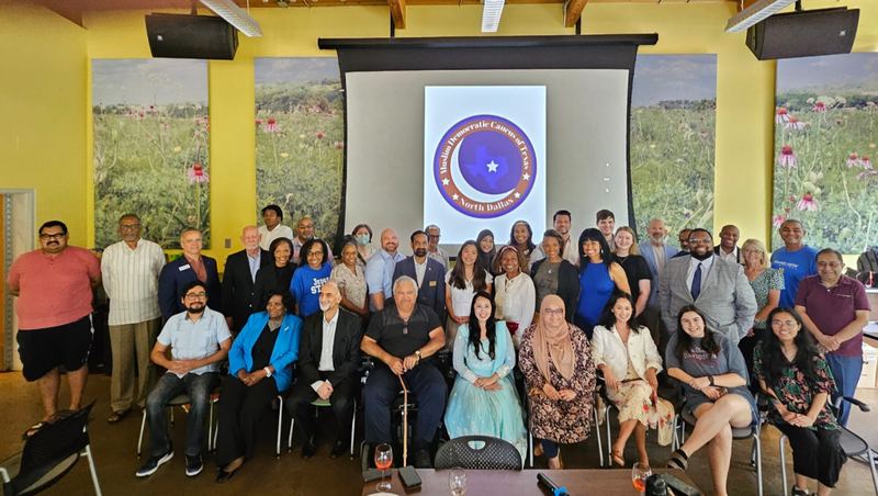 Roughly forty members, allies, and elected officials posed together in front of a screen showing the MDCND seal