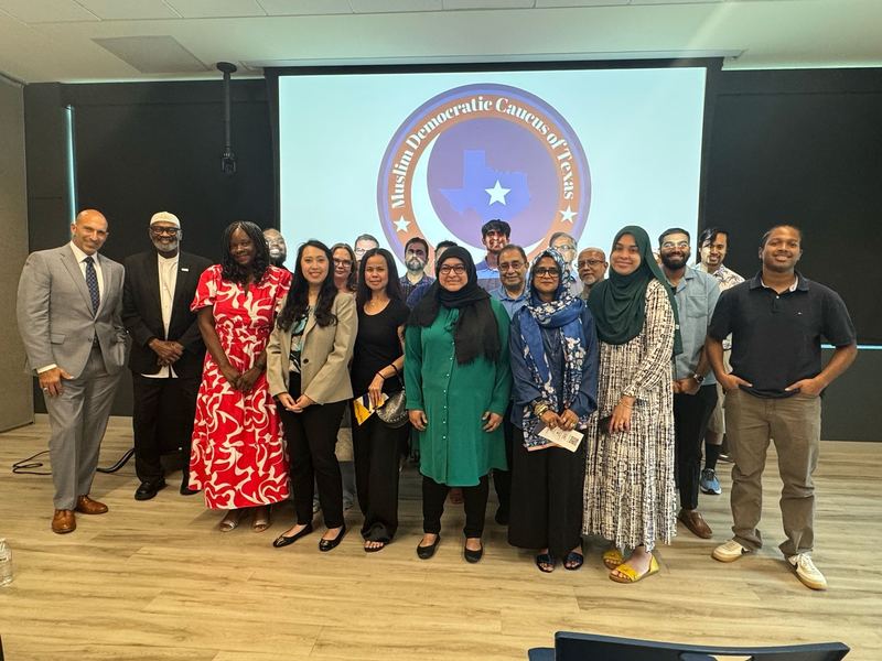 Around twenty members standing together in front of a projected Muslim Democratic Caucus of Texas seal