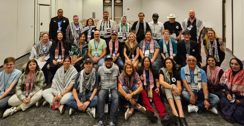 About thirty delegates in keffiyehs posed together in a convention meeting room