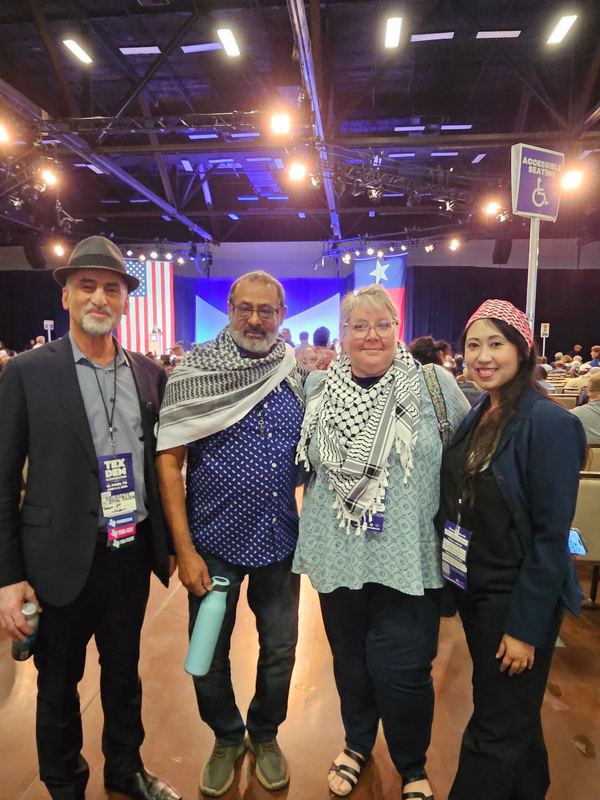 Four delegates with convention credentials standing on the convention floor in front of the main stage