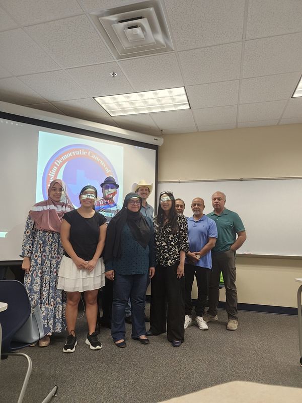 Nine members standing together in a meeting room in front of a projected caucus logo